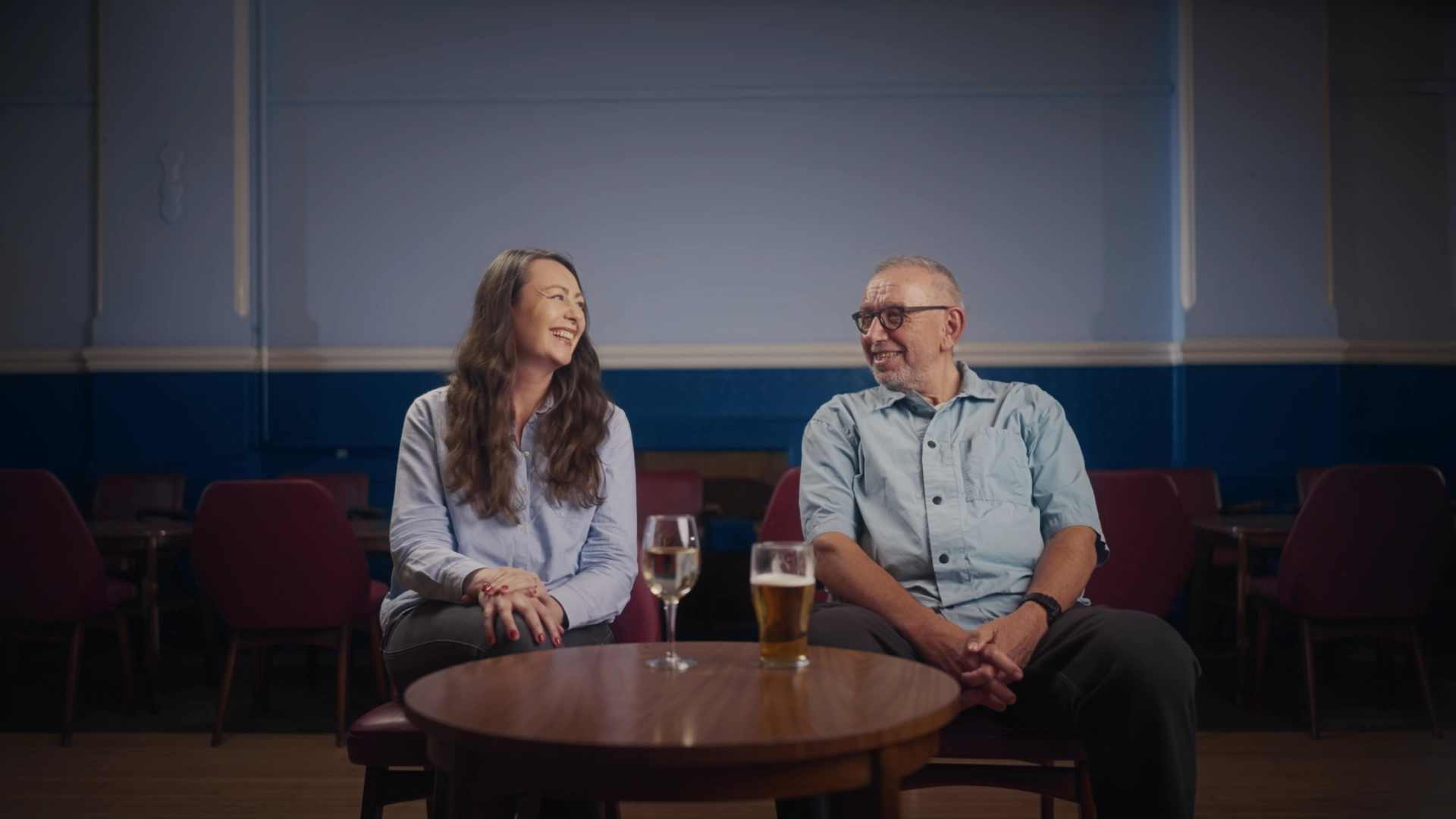 Two people laughing at a table with drinks in a working men’s club, from Dear Mr Manley