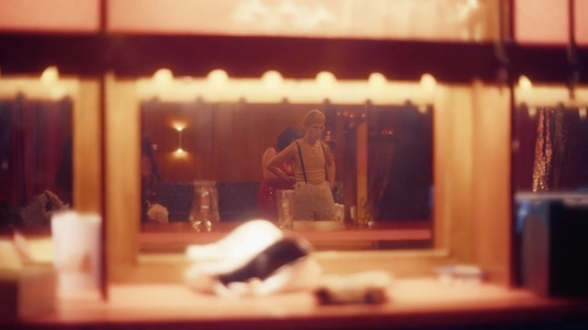 A performer in a yellow vest and braces reflected in a bulb-lit dressing-room mirror, from Dear Mr Manley